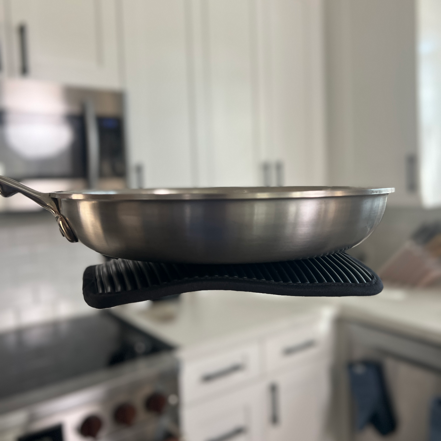 Stainless steel frying pan on a stovetop with a blurred kitchen background