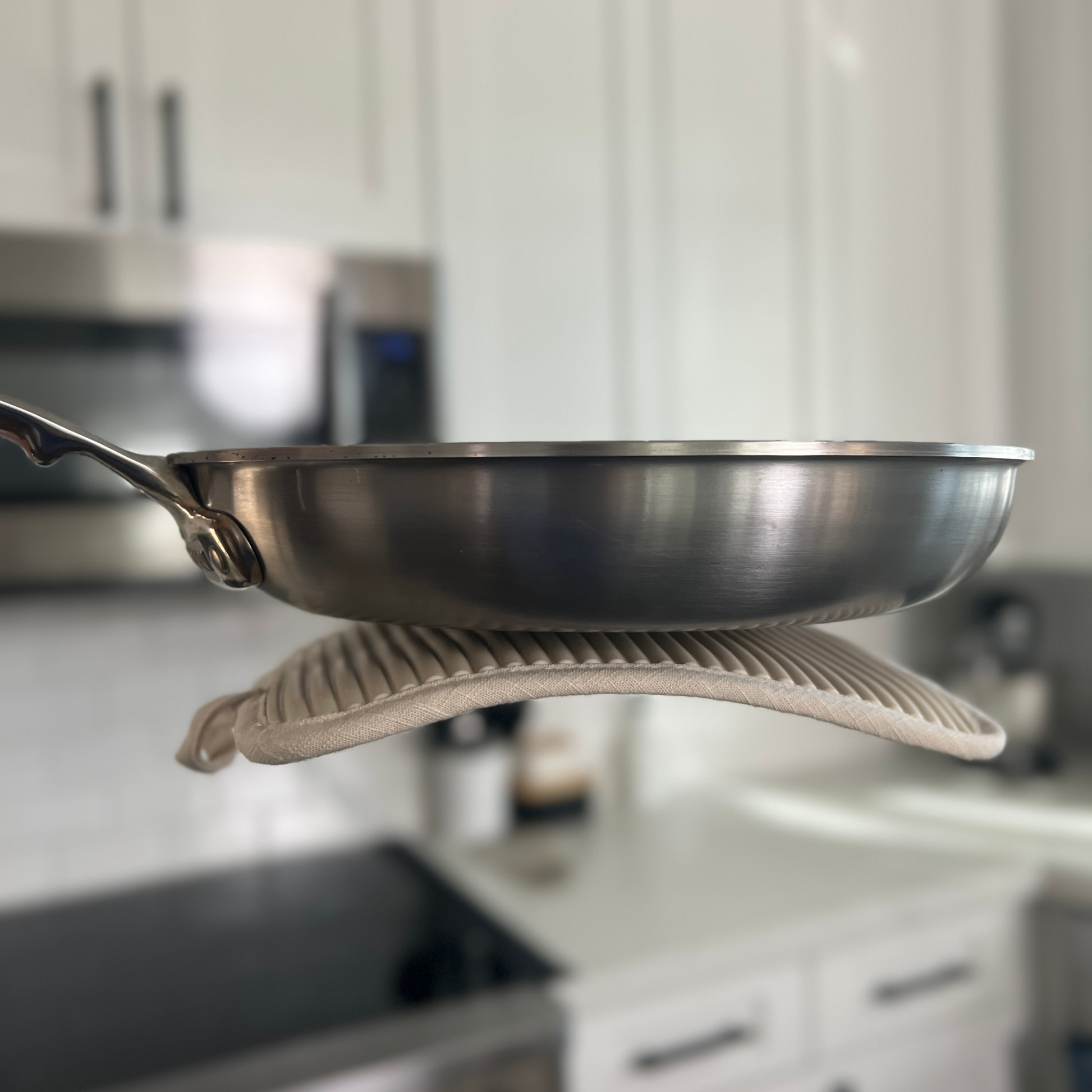 Stainless steel frying pan on a pot holder with a blurred kitchen background