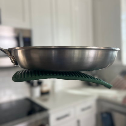 Stainless steel frying pan on a green pot holder with a blurred kitchen background