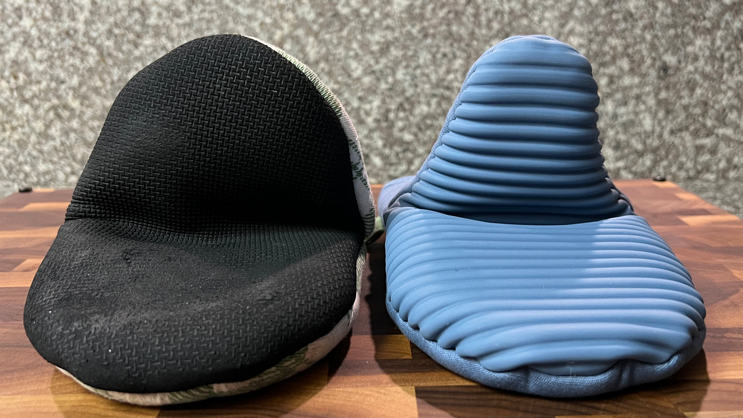 Black and blue oven mitts on a wooden surface with a gray background