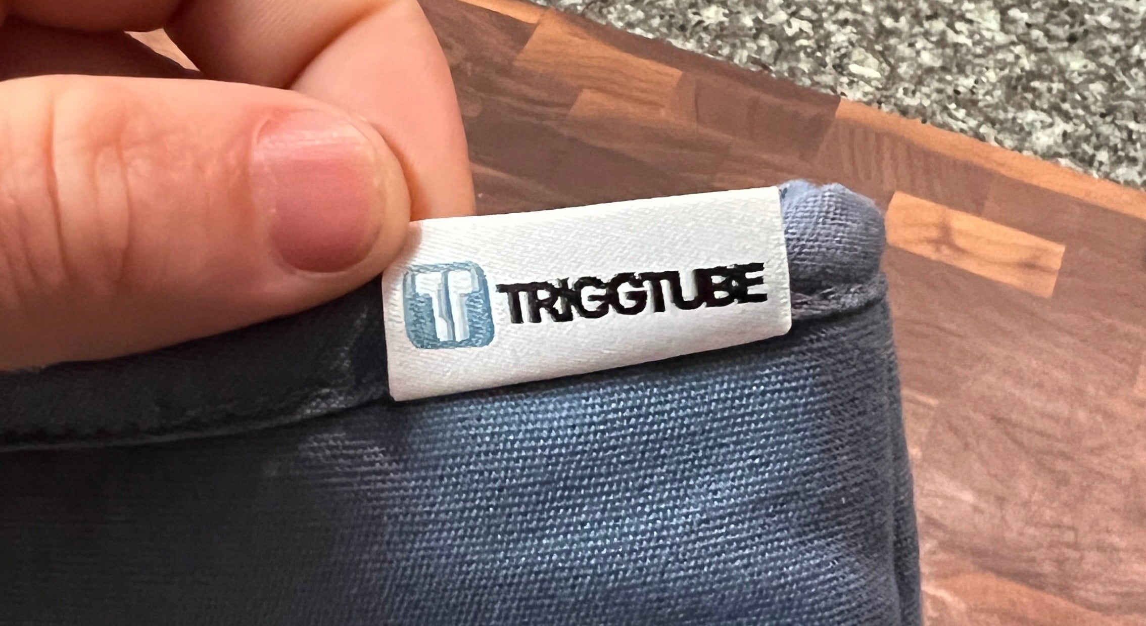 Triggtube label on a blue product with a hand holding it, against a wooden surface.