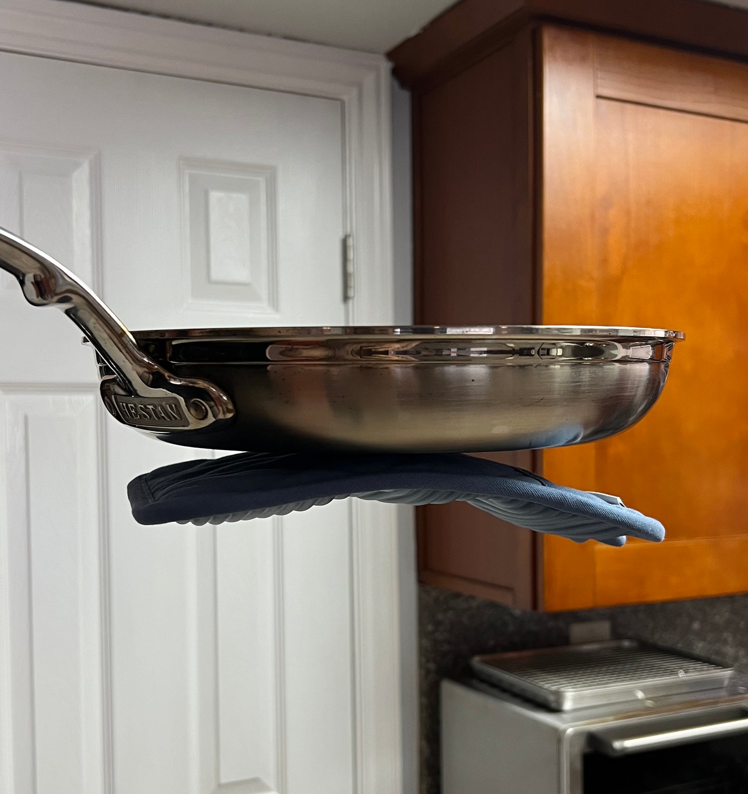 A magnetic hot pad hanging from a frying pan in the kitchen.