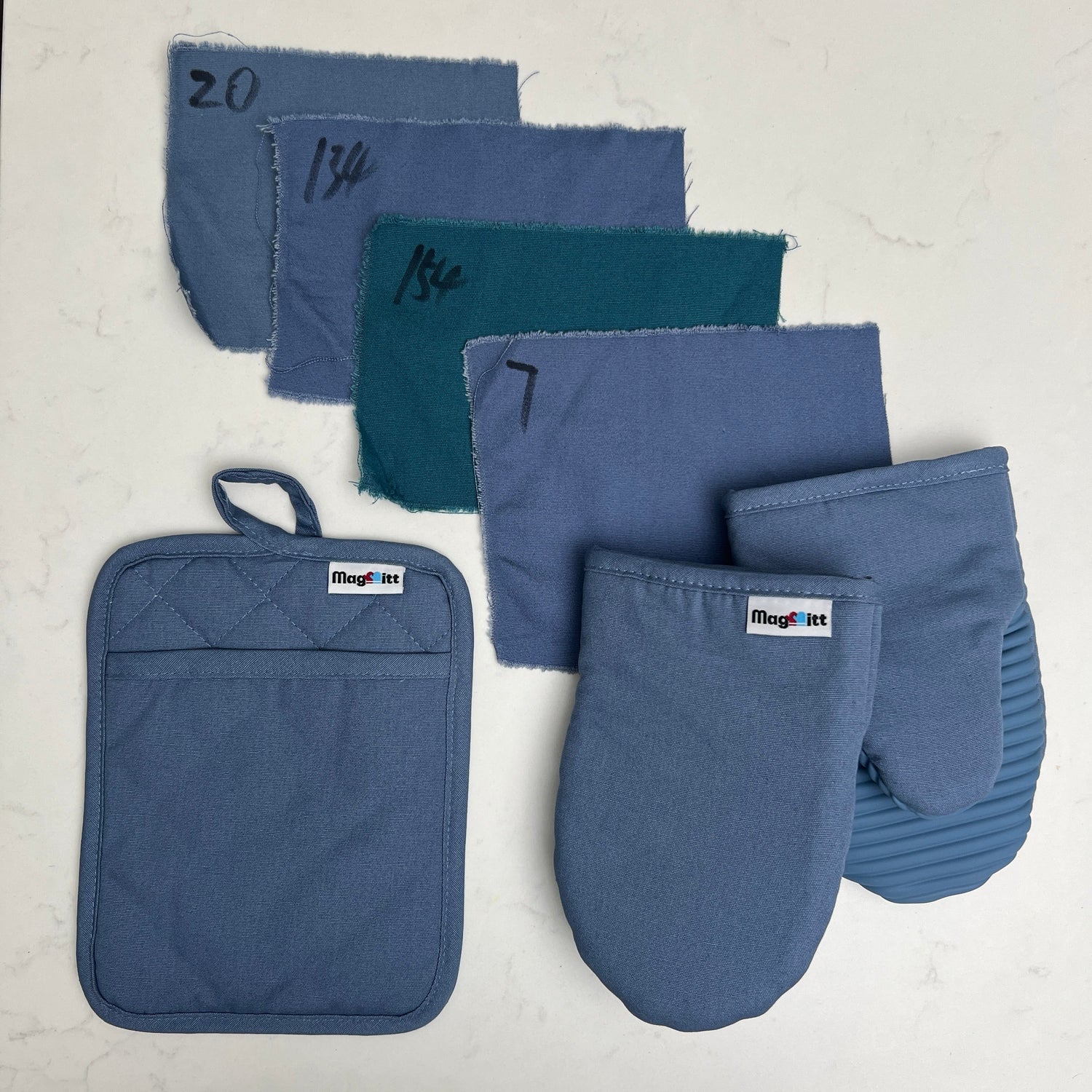 Set of blue kitchen mitts and potholders on a light gray background with fabric swatches