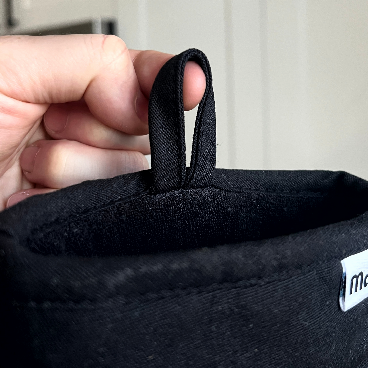 Person holding a black fabric loop with a visible brand logo.
