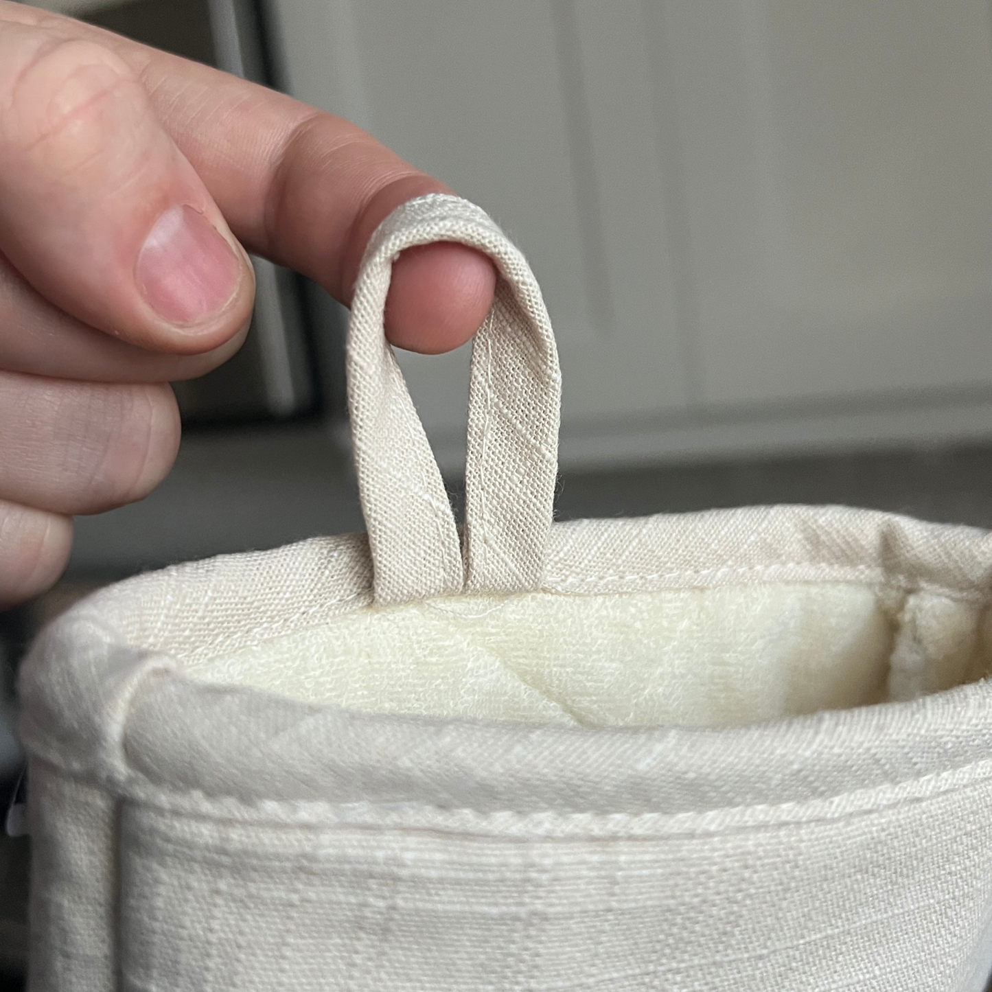 Hand holding a small beige fabric loop with a plain background