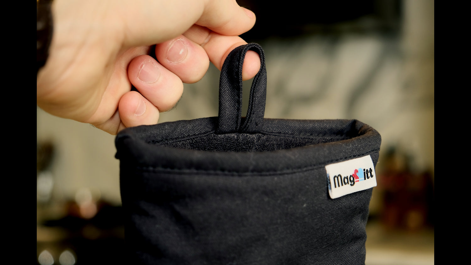 Black fabric bag with a visible brand label held by a hand against a blurred background